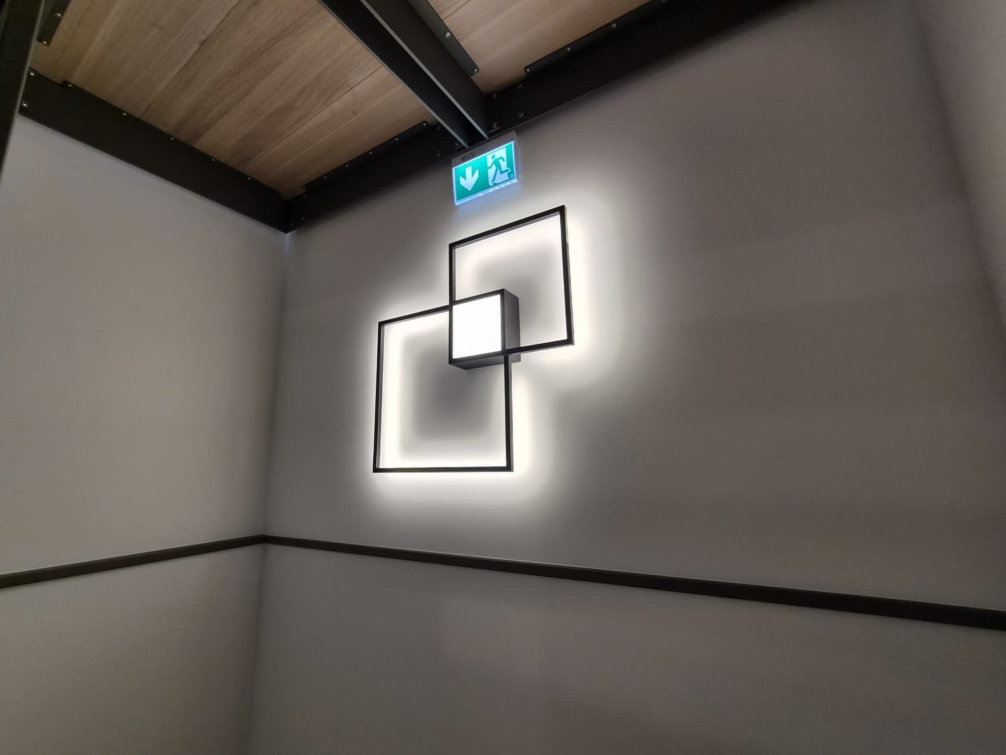 Applique lumineuse décorative formée de deux carrés, au-dessus d'une signalisation de sortie de secours